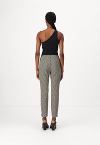 Zwarte top met één schouder, gecombineerd met zwart-witte gestreepte broeken. Een paar zwart leren sandalen met hakken maakt de outfit compleet.