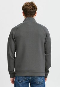 Gray zip-up sweatshirt with a high collar, long sleeves, and ribbed cuffs, paired with blue jeans. Smooth texture, minimal seams.