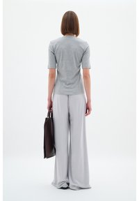 Szary, krótki top w połączeniu z luźnymi, jasnoszarymi spodniami. Modelka trzyma ciemnobrązową torbę. Gładkie tkaniny o luźnym kroju.