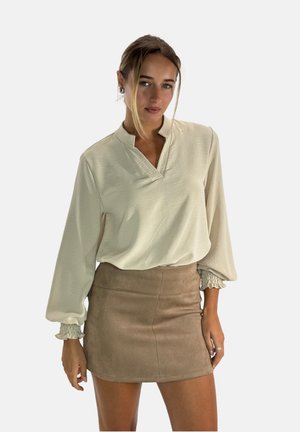 Blusa a maniche lunghe beige chiaro con scollatura a V e polsini arricciati, abbinata a una minigonna in suede color tan con una texture liscia.