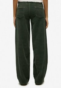 Pantalones de pana de pierna ancha en verde oscuro, con textura acanalada, bolsillos traseros y cintura alta con un dobladillo deshilachado.