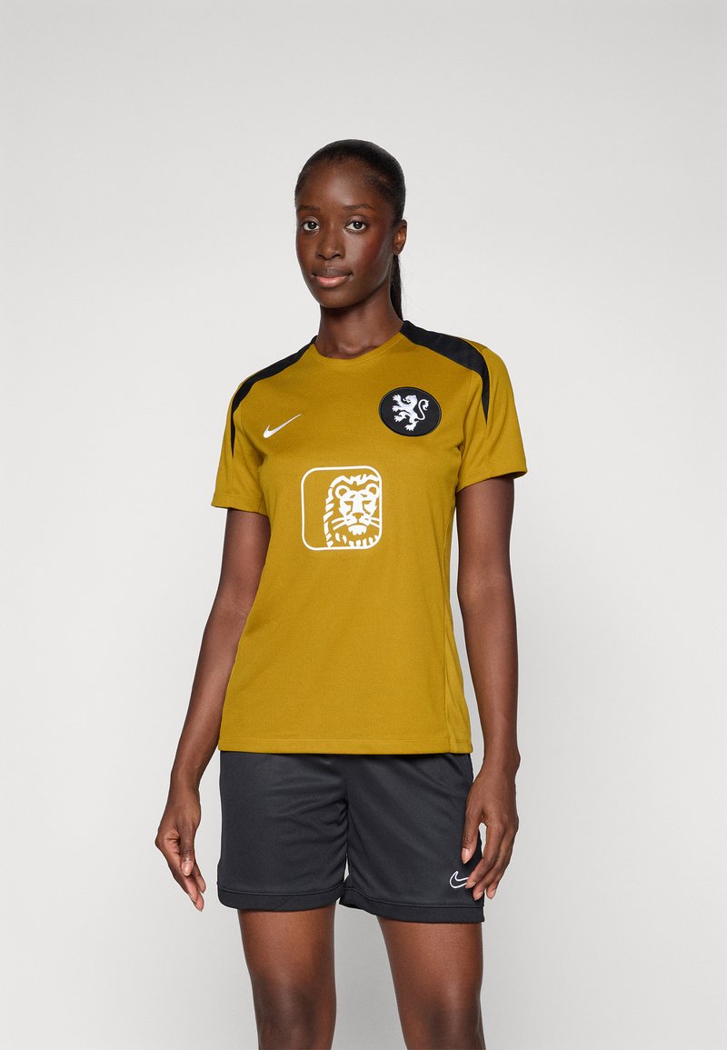 Geltona sportinė marškinė su juodais akcentais ir liūto emblemą, derinamos su juodais šortais, kuriuose balta „Nike“ logotipas. Lygus audinio paviršius.