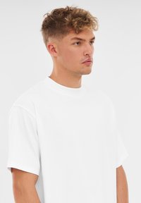 Vit bomulls T-shirt med rundad halsringning, korta ärmar och avslappnad passform. Slät textur, inga synliga mönster eller dekorer.