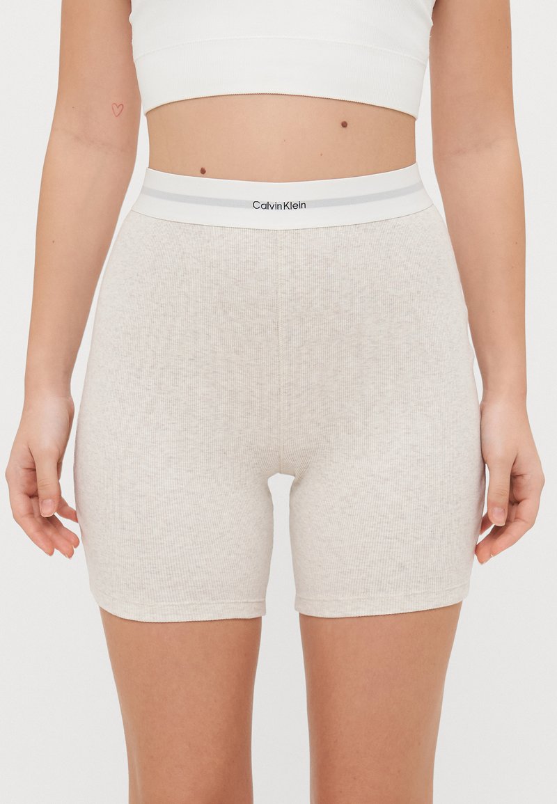 Calvin Klein šviesiai rudos spalvos juostos šortai su pilku juosmeniu, ant kurio matomas prekės ženklas. Medžiaga atrodo minkšta, o dizainas prigludęs.
