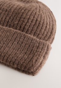 Brown knitted beanie made of soft wool. Features a folded cuff and textured ribbing throughout. Compact, warm, and versatile design.