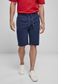 Marineblauwe katoenen shorts met een elastische tailleband, trekkoord en zijzakken. Draag het met een rood T-shirt met korte mouwen en witte sneakers.