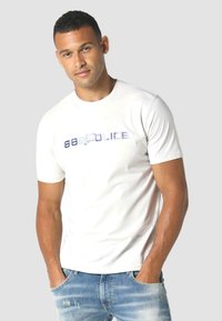 Bijela majica kratkih rukava sa plavim metalik logotipom "883 Police" na prsima; kombinirana s plavim izdrikanim trapericama.