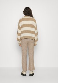 Pull oversize rayé beige et crème avec tissu texturé, associé à un pantalon beige en maille ajusté et des chaussures épaisses à semelles noires.