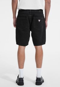 Pantaloni scurți din denim negru cu un croi drept, având două buzunare la spate și o pată de logo triunghiulară. Bază standard și detalii minime de uzură.