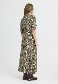 Robe imprimée léopard avec de courtes manches bouffantes et une silhouette longue. Fabriquée en tissu doux, elle offre une texture fluide et une fente sur le côté. Bottes marron à cheville.