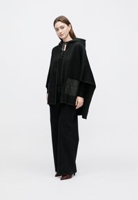 Mustast ponchost, millel on tikitud tasku, kapuuts ja tõmblukuga kinnis. Kandmisel musta t-särgi ja laiade säärega pükstega, millega on seljas terava ninaga kontsakingad. Siidine tekstuur.