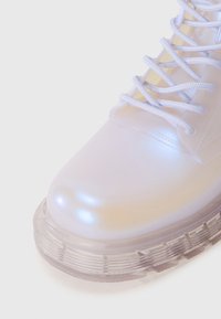 Transparent, glossy boot with a rounded toe, light blue laces, and a clear, textured sole featuring layered ridges.