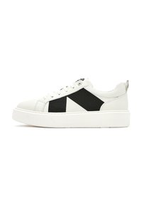Baskets blanches avec des accents en tissu noir, présentant une semelle épaisse, un bout rond et un système de laçage. Notez le motif triangulaire distinctif.
