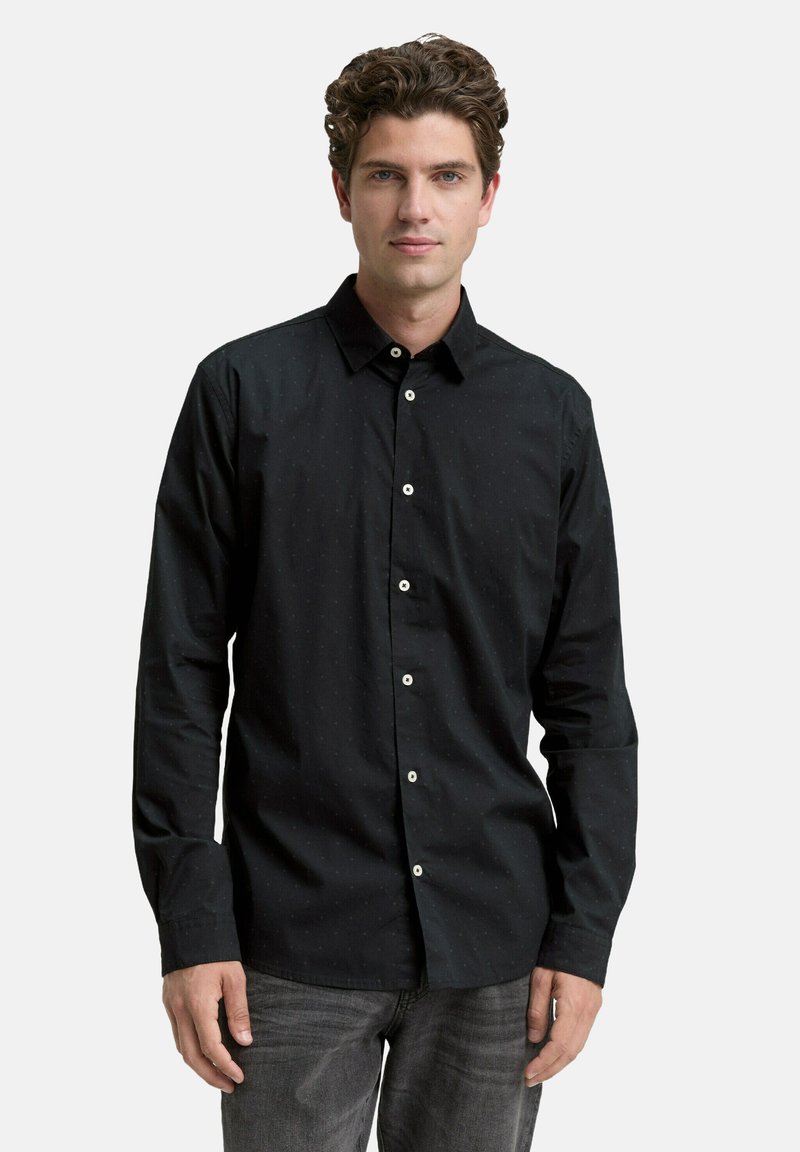 Black button-up shirt with subtle dot patterns, long sleeves, a collar, and white buttons, paired with dark grey jeans.