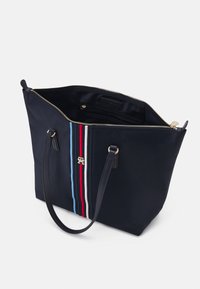 Sac cabas bleu marine avec poignées noires, rayures verticales rouges, blanches et bleues, fermeture éclair dorée et poche intérieure zippée.