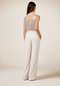Haut en sequins argentés brillants avec un dos en V, associé à un pantalon large blanc taille haute. Texture de tissu lisse tout au long.