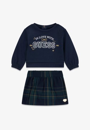 Haut à manches longues bleu marine avec le texte « In Love With GUESS » associé à une jupe à carreaux bleu marine et vert avec un petit logo en forme de cœur.
