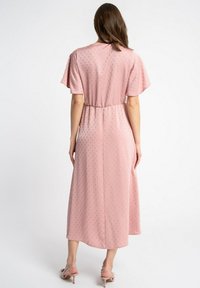 Różowa sukienka midi z teksturowanym wzorem, krótkimi, falbaniastymi rękawami i dopasowanym pasem w talii. Noszona z jasnoróżowymi sandałami na obcasie.