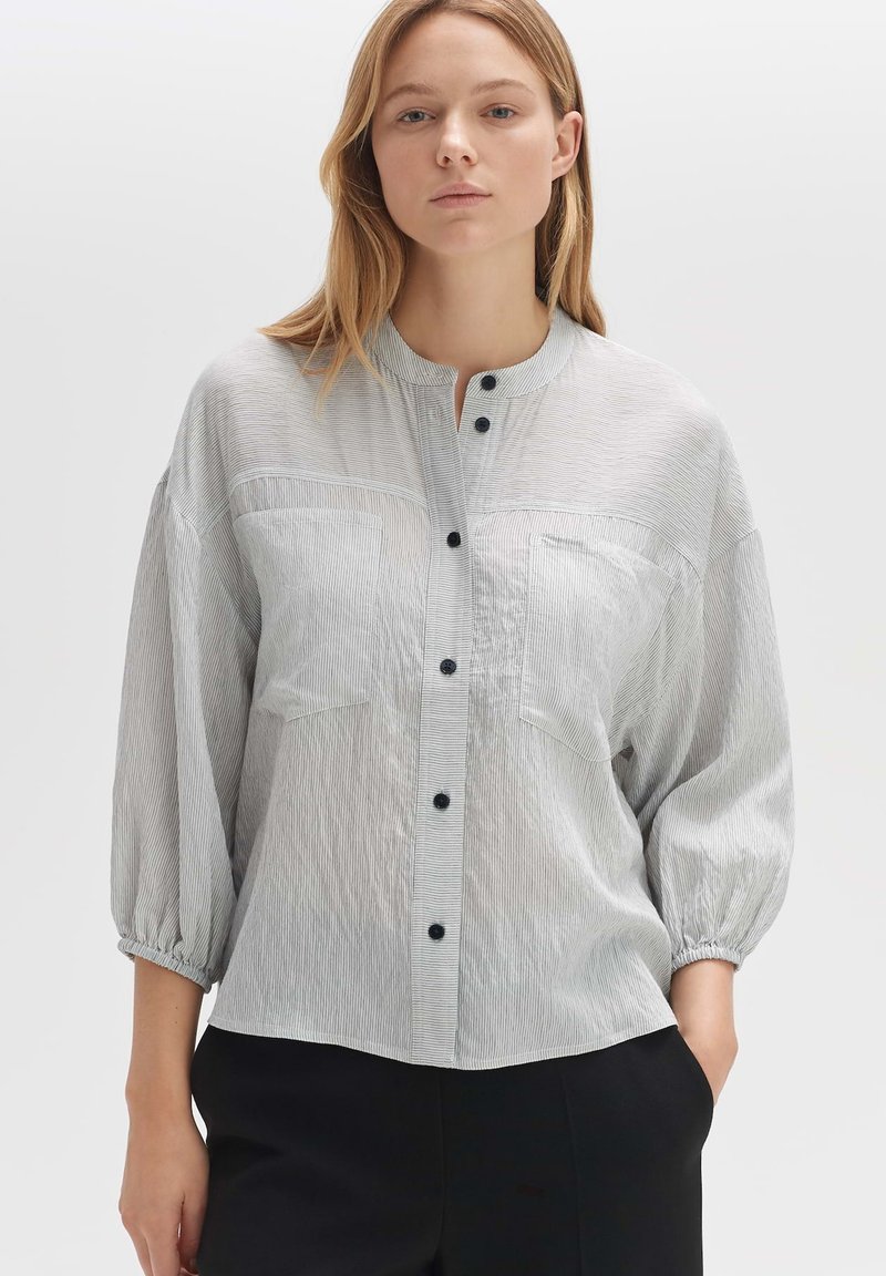 Light grey button-up shirt with vertical dark stripes, rounded collar, two chest pockets, and gathered balloon sleeves. Textured fabric.