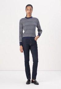 Marineblauw en witte gestreepte trui met een ronde hals en geribbelde manchetten, gecombineerd met donkere jeans en zwarte schoenen. Eenvoudig, getailleerd ontwerp.