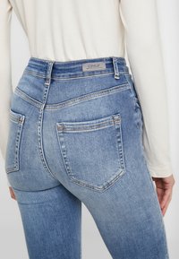 Jeans de mezclilla azul claro con cintura alta, que cuentan con bolsillos traseros, un ligero efecto de desvanecimiento y una etiqueta de marca en la cinturilla.
