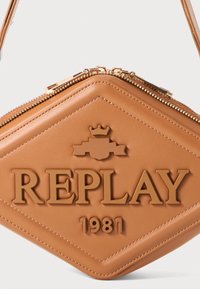 Tan lærveske med diamantform, preget "REPLAY" og krone-logo, doble gullglidelåser og en jevn tekstur.