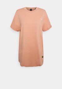 Světle broskvové tričko vyrobené z bavlny, s kulatým výstřihem, krátkými rukávy a malým logem na hrudi. Na spodním lemu je opatřeno štítkem.