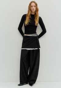 Sort langærmet top kombineret med løse sorte bukser. Bemærkelsesværdigt gråt stribet linningdetalje og spidse sorte sko. Glat stoffinish.