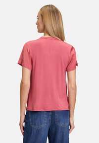Kortärmad rosa t-shirt med avslappnad passform, rund halsringning och slät textur, tillsammans med blå denimbyxor med synliga fickor.