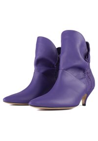 Par de botas de cuero púrpura hasta el tobillo con punteras puntiagudas, diseño de parte superior holgada y tacones bajos tipo kitten, sobre un fondo blanco.