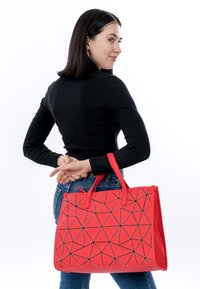 Borsa geometrica rossa con motivi neri, realizzata in materiale durevole. Presenta due manici superiori e una chiusura a zip.