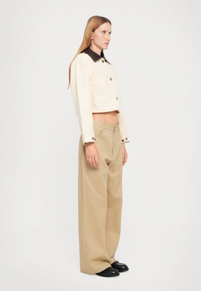 Jachetă din denim bej cropped cu guler negru, asociată cu pantaloni bej lejeri cu modele fine de puncte și pantofi negri.