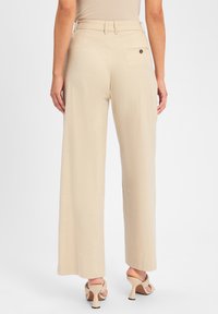 Beige wijde stoffen broek in lichtgewicht materiaal met een gladde textuur. Met een achterzak met een knoopsluiting.