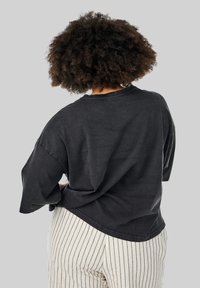 Sort oversized bomulds t-shirt med rund halsudskæring, sænkede skuldre og en buet kant. Stoffet ser blødt og let tekstureret ud.