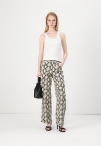 Pantalones de pierna ancha en un estampado de serpiente beige, combinados con una camiseta sin mangas blanca. Los accesorios incluyen un bolso negro y tacones abiertos con estampado.