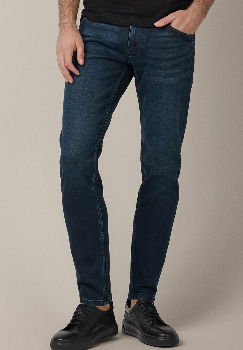 Mrocznie niebieskie dżinsy o slim fit, z delikatnym efektem sprania, klasycznym pięciokomorowym designem, w połączeniu z czarnymi trampkami.