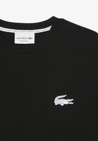 Sweatshirt de algodão preto com um logo de crocodilo branco no lado esquerdo do peito, gola canelada e textura suave.