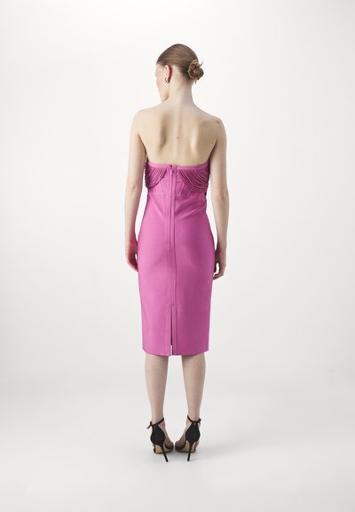 Fitted pink dress with a straight silhouette, decorative ruching at the back, and a back zip; paired with black high-heeled shoes.