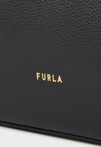 Crna kožna torba s teksturiranom površinom, s markom "FURLA" ispisanom zlatnim slovima. Jednostavan i minimalistički dizajn.
