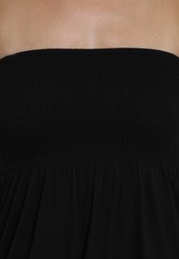 Zwart strapless jurk van gladde stof met een gerimpelde corsage en losse, vloeiende rok. Heeft een gathered taille en een gestructureerd oppervlak.