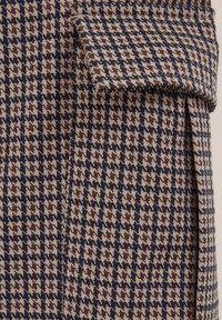 Villa sekoitusmateriaali, joka on varustettu ruskeasävyisellä ja laivastonsinisellä houndstooth-kuviolla, sisältää käänteet kauluksessa ja teksturoidun pinnan.