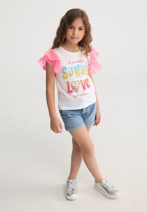 T-shirt bianca con testo stampato colorato "SUNNY LOVE", maniche ruffle rosa, abbinata a pantaloni shorts di jeans e sneakers argentate.