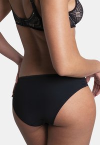 Bas de bikini noir avec une texture lisse et une coupe classique, doté d'une taille haute et de coutures minimales pour un apparence sans couture.