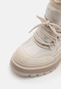 Bottes en suède beige et métallique avec des accents de strass, semelle en caoutchouc épaisse et lacets en tissu. La partie supérieure présente un design texturé et des détails de couture.