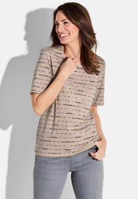 Beige gestreiftes T-Shirt mit kurzen Ärmeln, mit feinen blauen und dunkelgrauen Streifen. Weicher Stoff mit lockerer Passform. Kombiniert mit grauen Jeans.