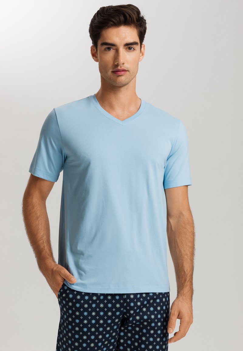 Camiseta de pico azul claro hecha de material suave, con mangas cortas. El modelo lleva pantalones oscuros de rayas azules con un pequeño diseño geométrico.