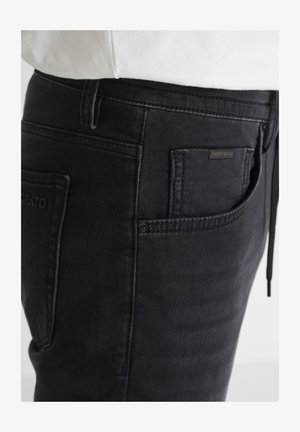 Primo piano di jeans in denim nero indossati con una maglietta bianca, che mostra le tasche anteriori e posteriori con dettagli di cucitura visibili.