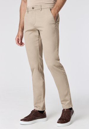 Beige chinos with a slim fit, cotton material, front pockets, and a single button closure, paired with dark brown sneakers.