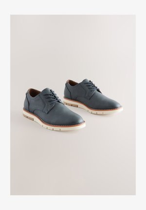 Scarpe eleganti da uomo in pelle blu con finitura liscia, caratterizzate da punta arrotondata, chiusura frontale con lacci e suola bianca con dettagli marroni a contrasto.