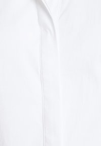 Vit skjorta med knappar i en mjuk, lätt tyg med klassisk krage och en subtil glans. Inkluderar en knappslå med diskreta stygn.